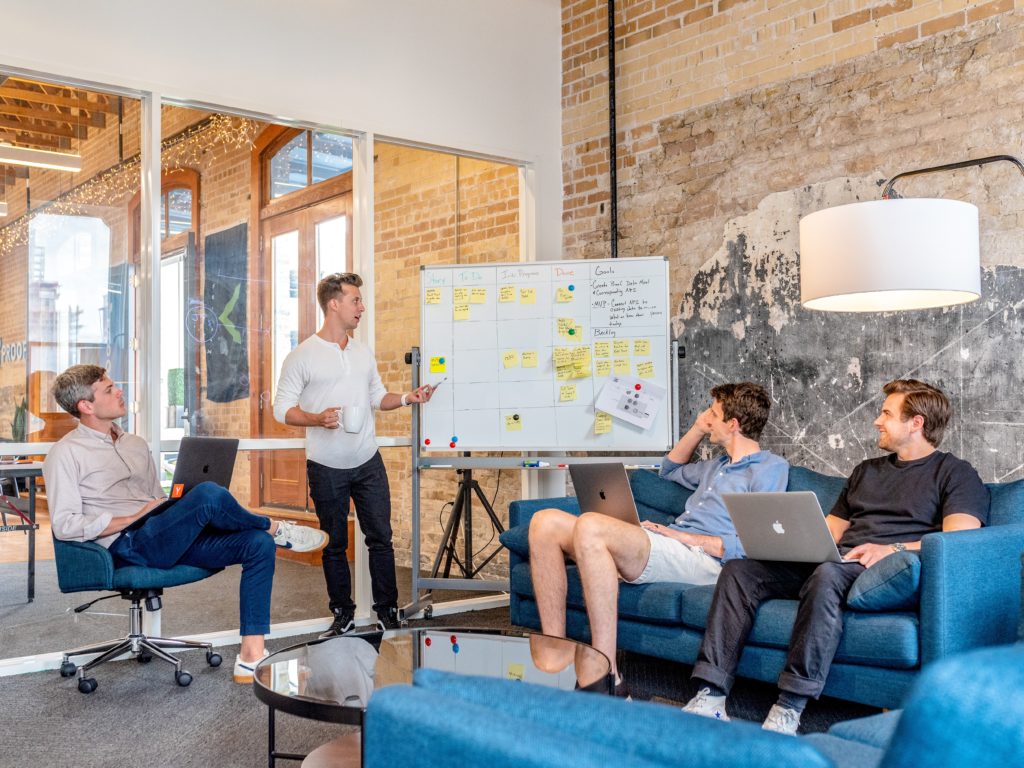 Group of people around a white board planing. Planning new features and changes is a critical piece to be managed in a good Software Maintenance Plan